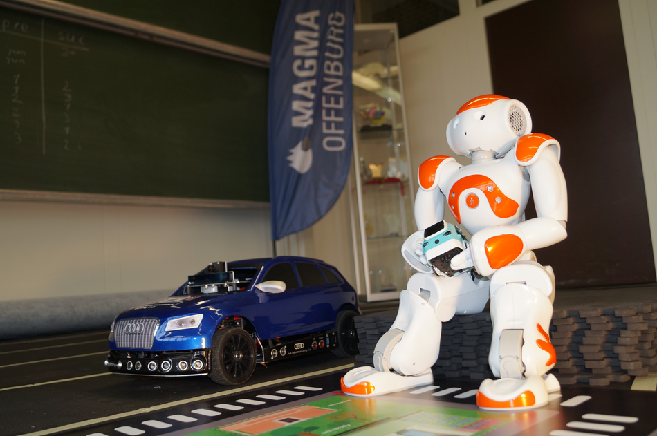 Nao-Roboter steht rechts neben Auto aus dem Audi-Cup